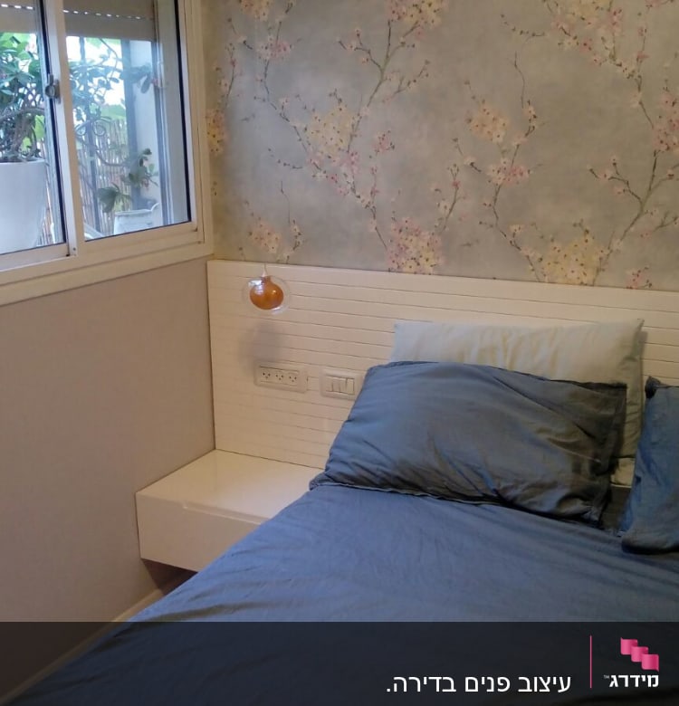 מיטה עם כריות כחולות וטפט פרחוני על הקיר